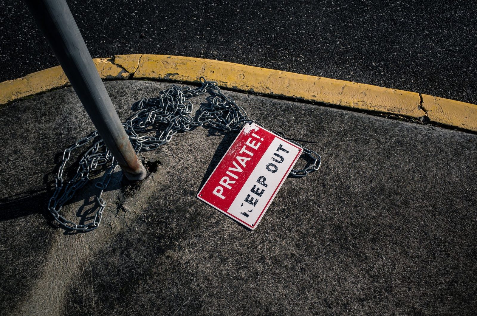 A chained "Private Keep Out" sign lies on an urban sidewalk, suggesting security and restricted property.