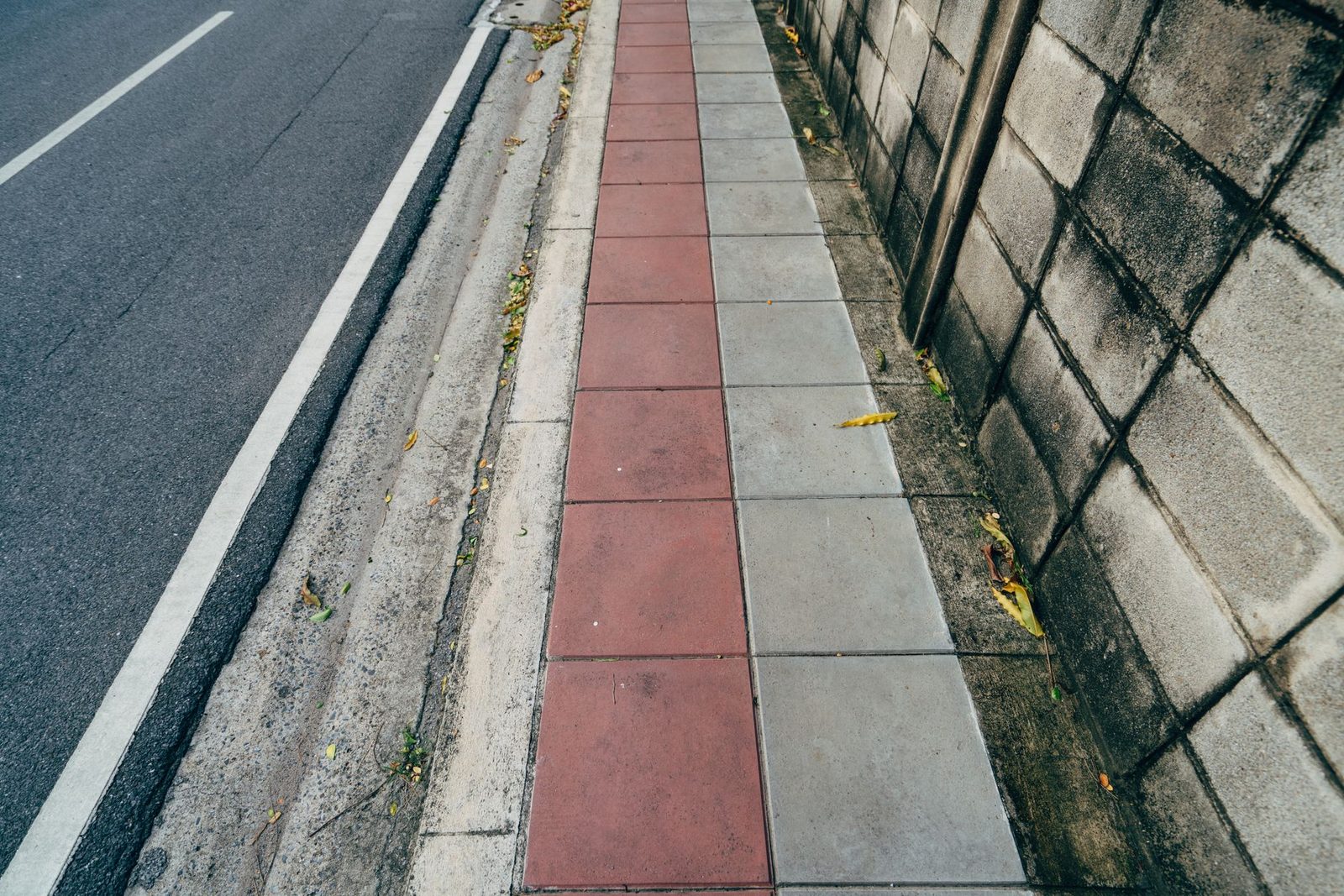 A colorful urban sidewalk runs beside a textured wall.