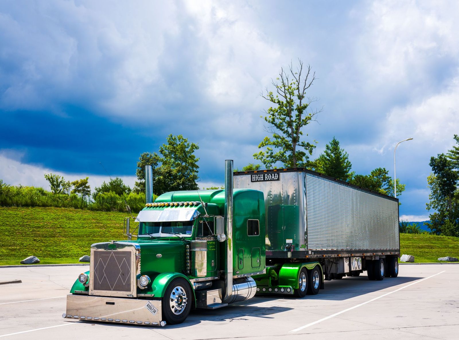 A green semi-truck parked outdoors under a dramatic cloudy sky.