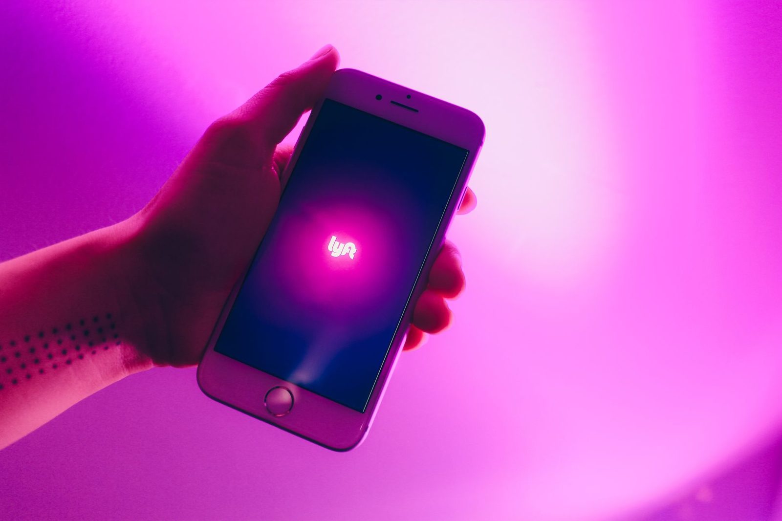 Una mano sostiene un teléfono con la aplicación de Lyft sobre un fondo rosa brillante.