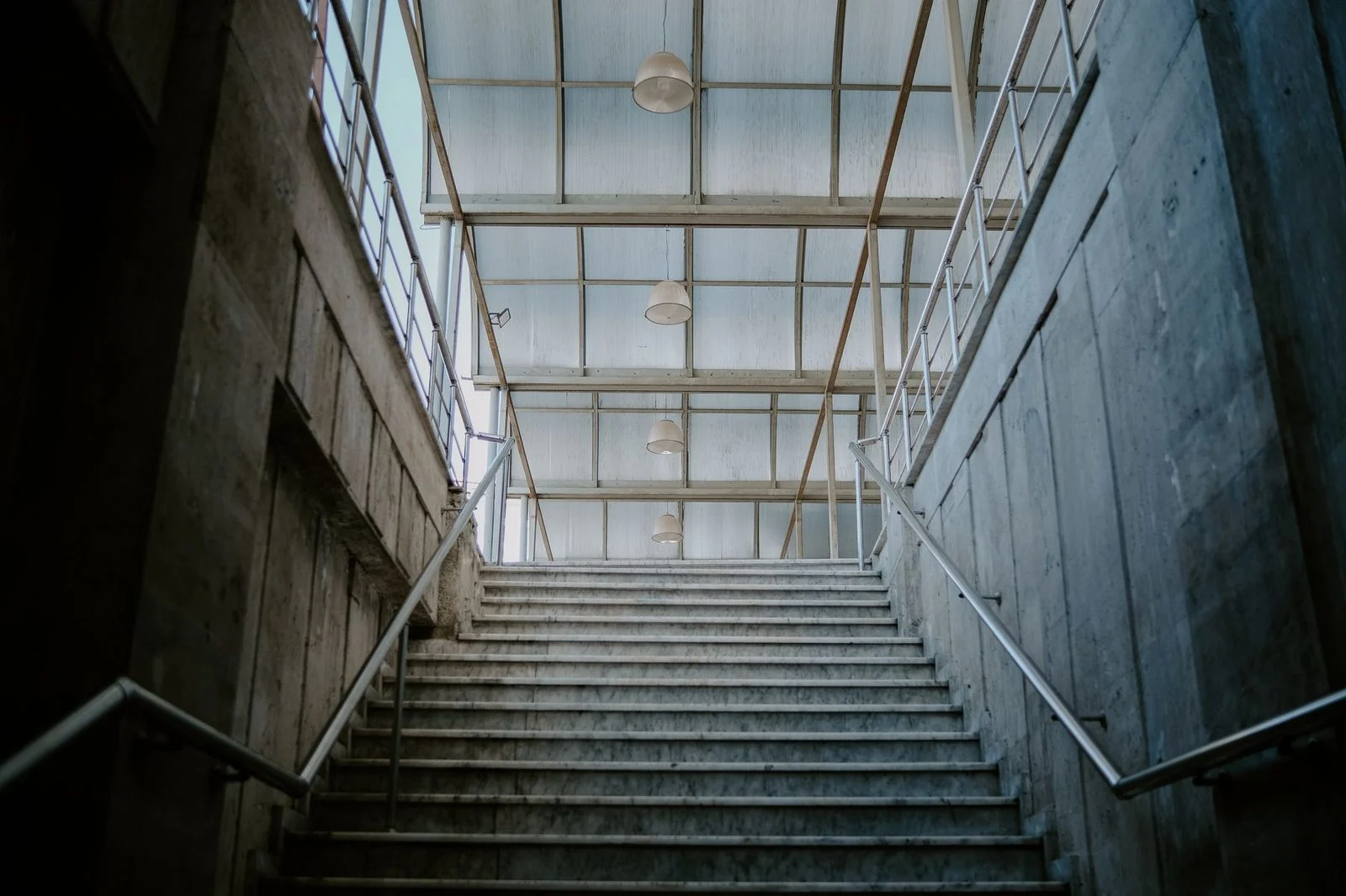 A modern indoor staircase with concrete walls and metal railings leading upward.