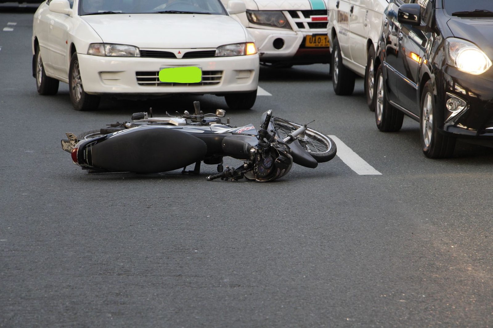 Motocicleta tendida en el suelo de una calle urbana con tráfico cerca tras un accidente.
