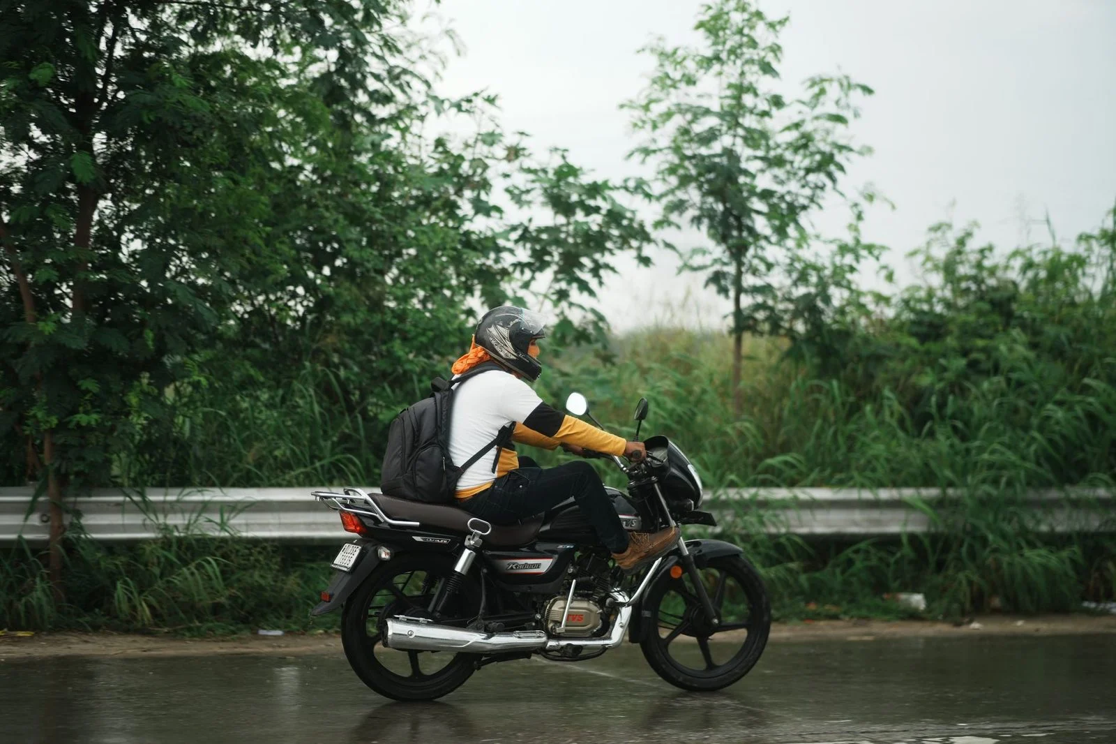 A rider on a motorcycle travels down a wet road on a rainy day.
