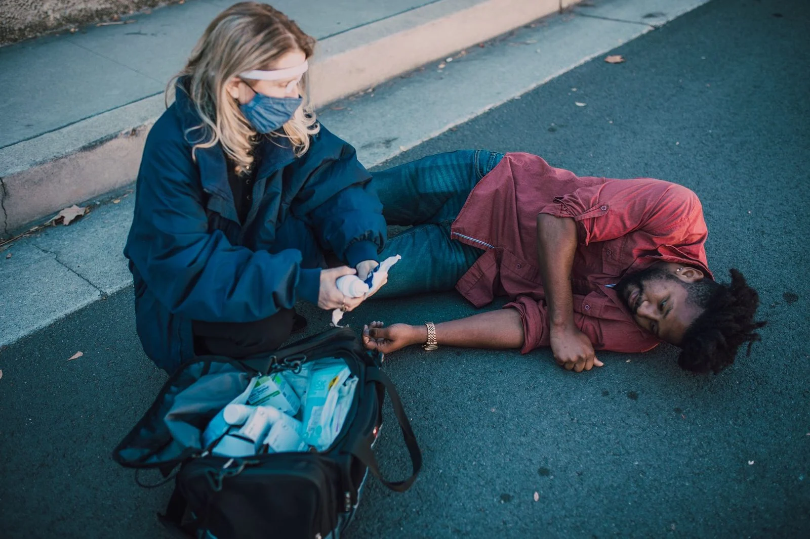 A paramedic gives first aid to an injured man lying on the side of the road.