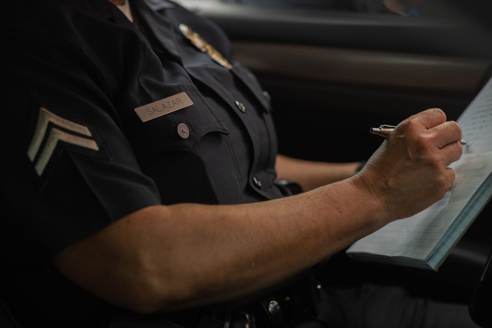 A police officer writes in a notebook while seated in a patrol car.
