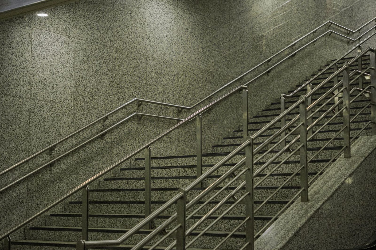 A sleek indoor staircase with polished metal railings and stone walls.
