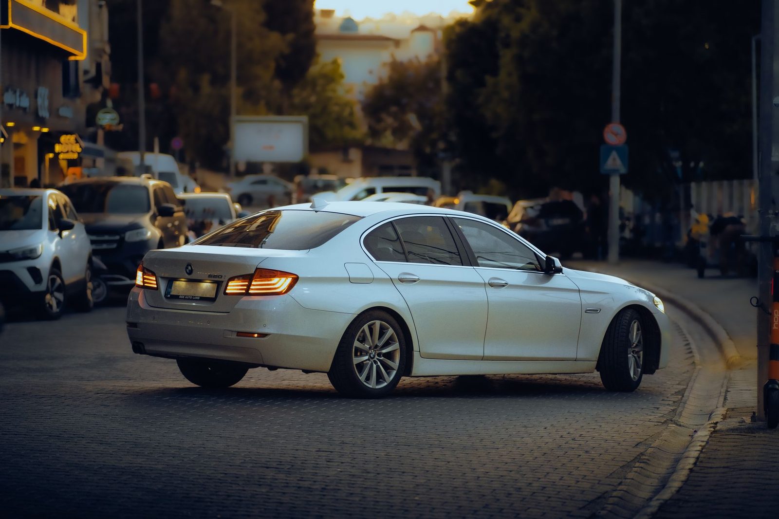 A white BMW sedan driving down a city street at twilight.