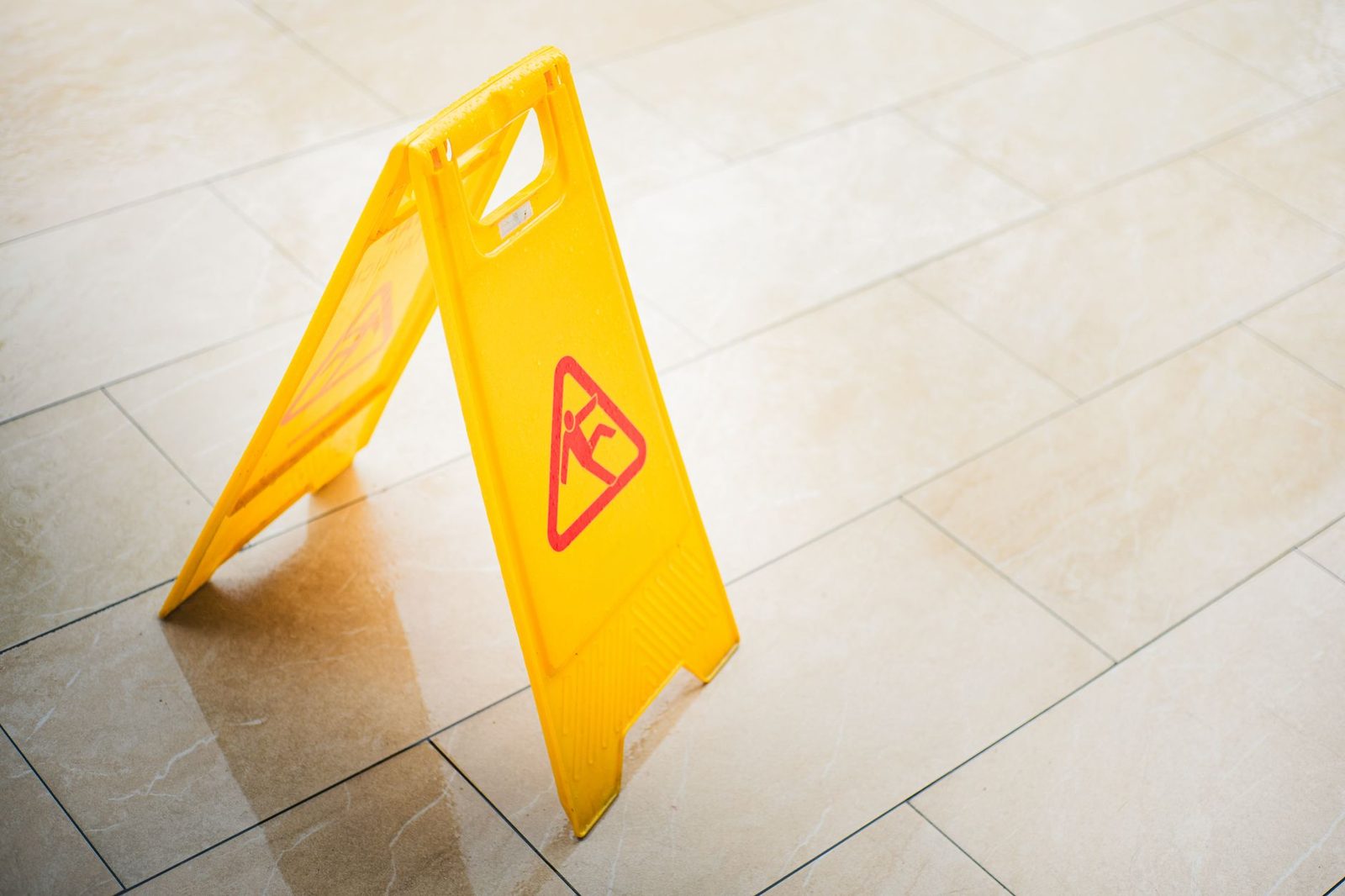 A yellow caution sign warns of a wet tiled floor in a commercial hallway.