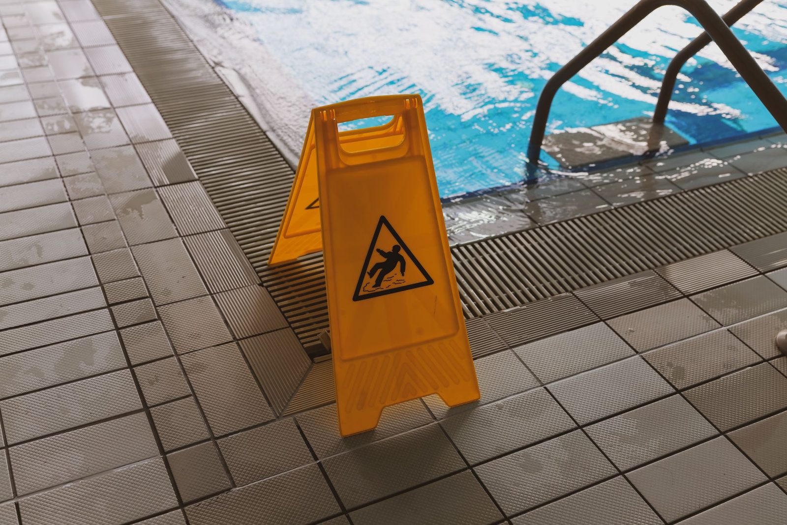 A yellow caution wet floor sign stands beside a swimming pool deck.