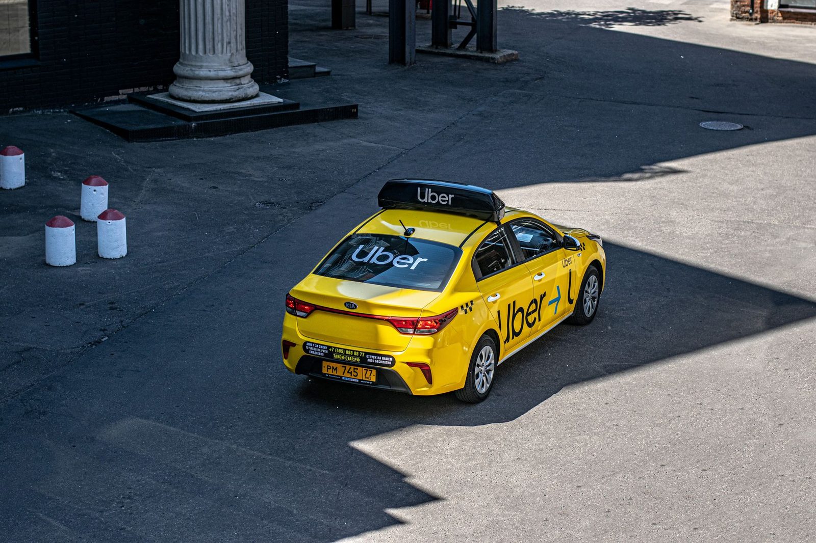 A yellow Uber taxi drives down a city street, photographed from above.