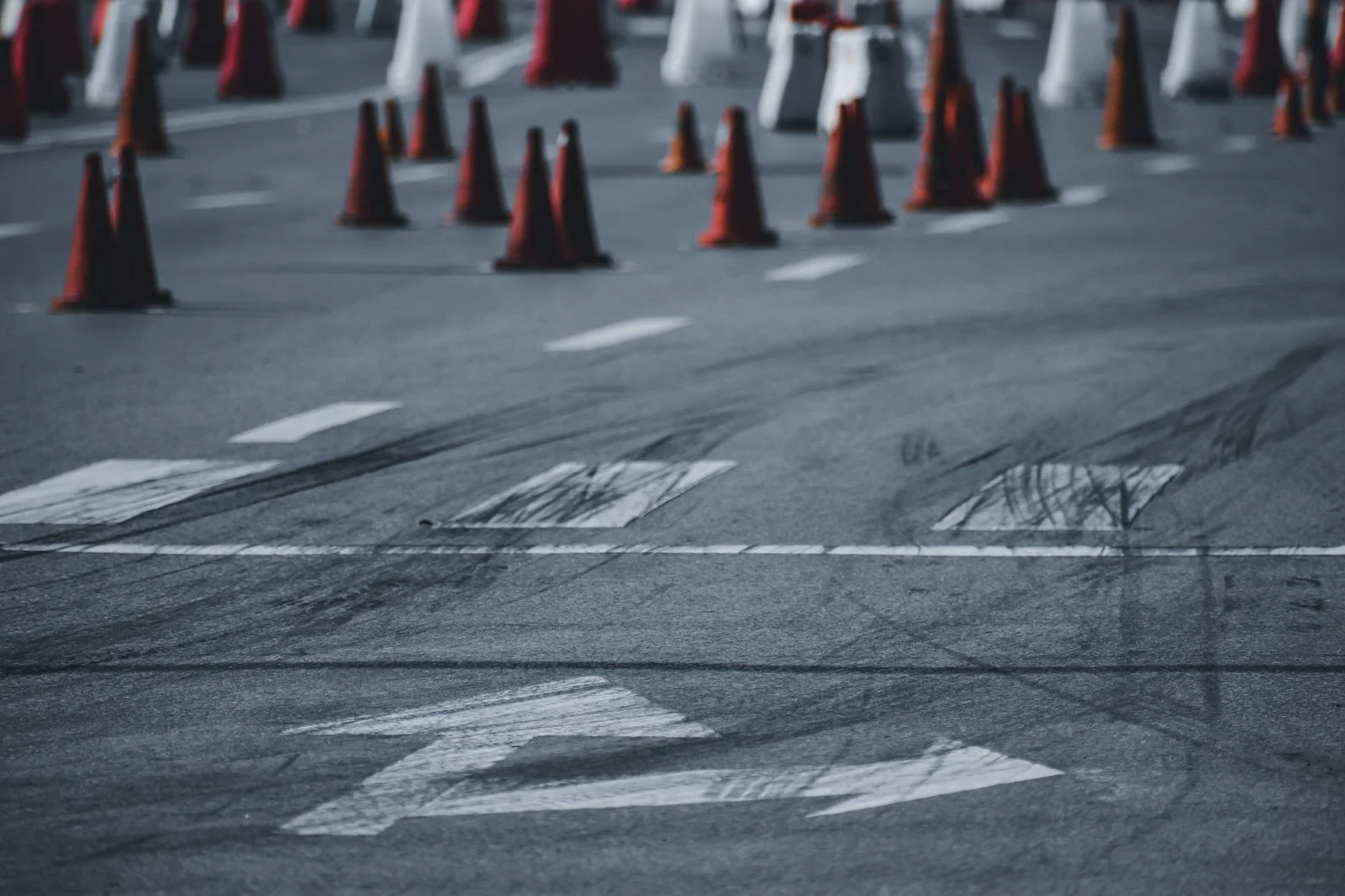 Asphalt city street with black tire tracks and red traffic cones in daytime.