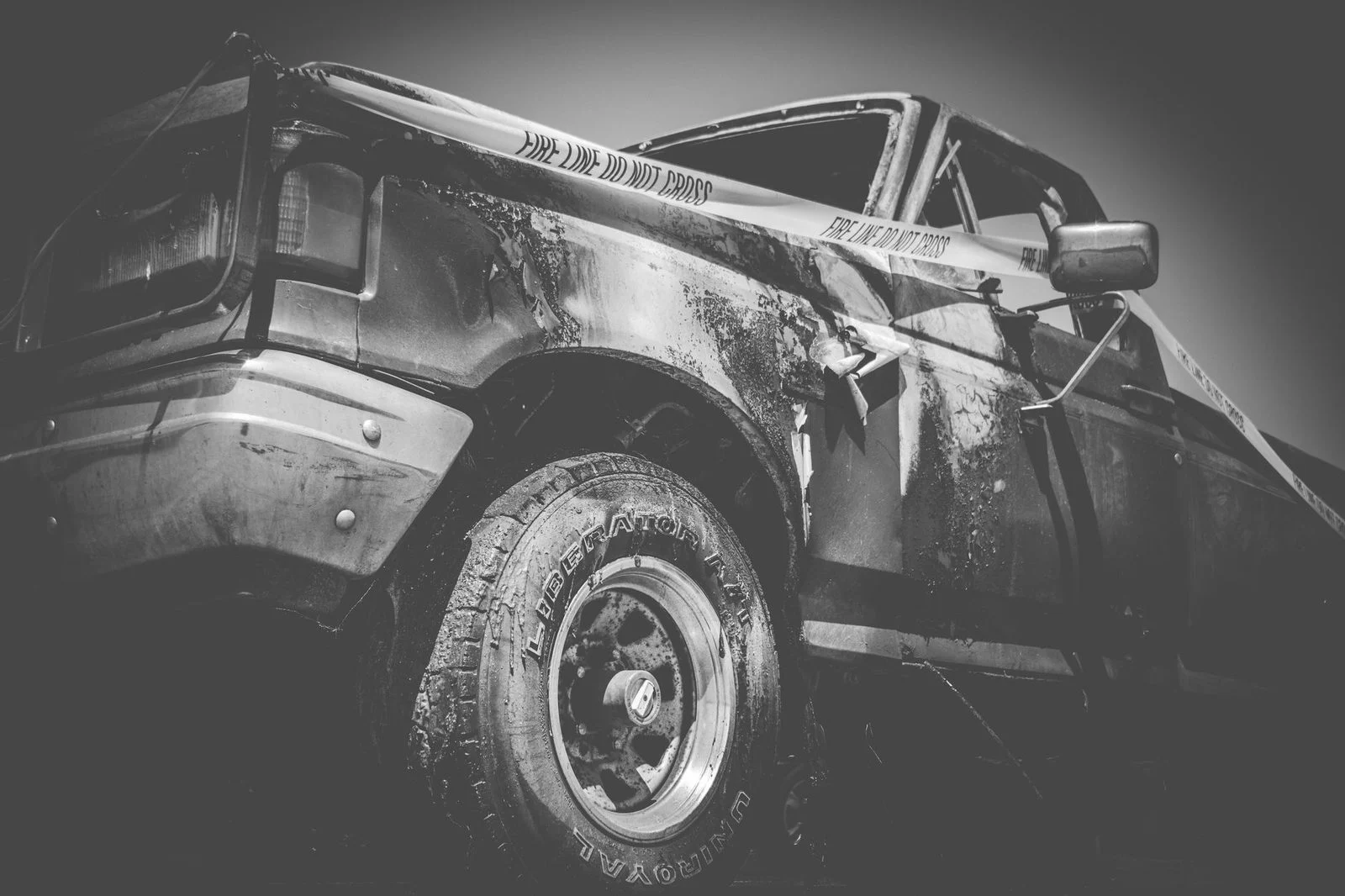 Black-and-white photo of a damaged truck behind yellow police tape at an accident scene.