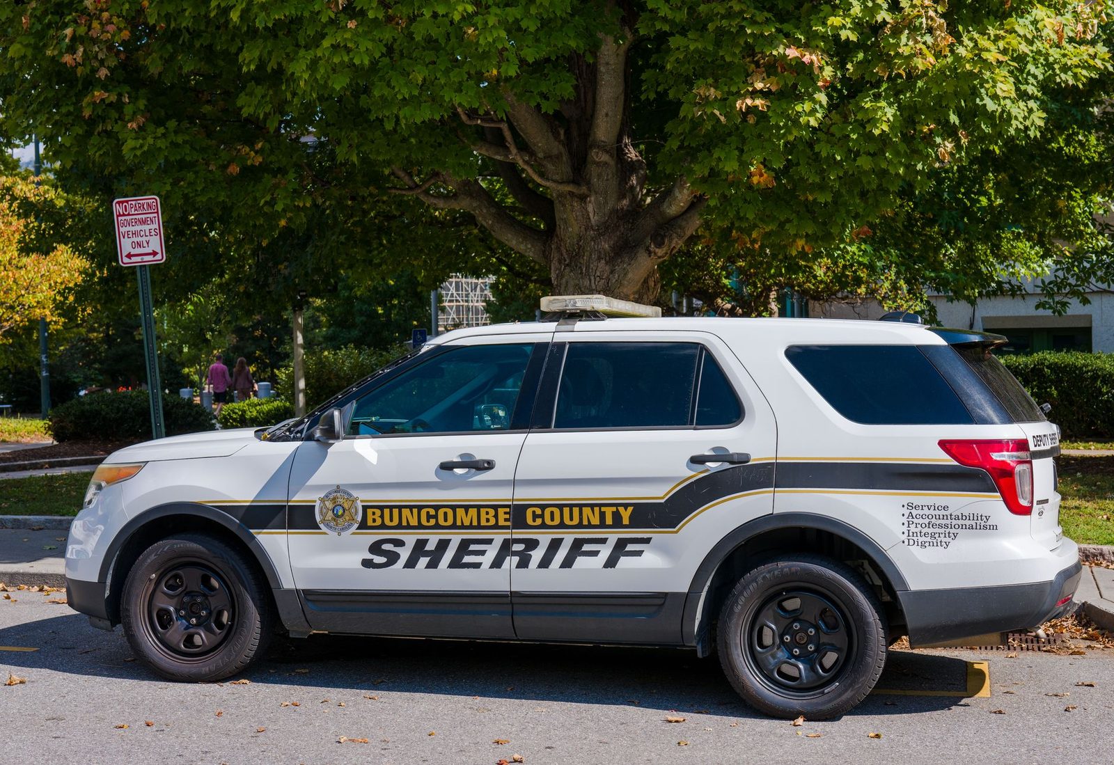 Buncombe County Sheriff's SUV parked on a street beside a large tree on a sunny day.