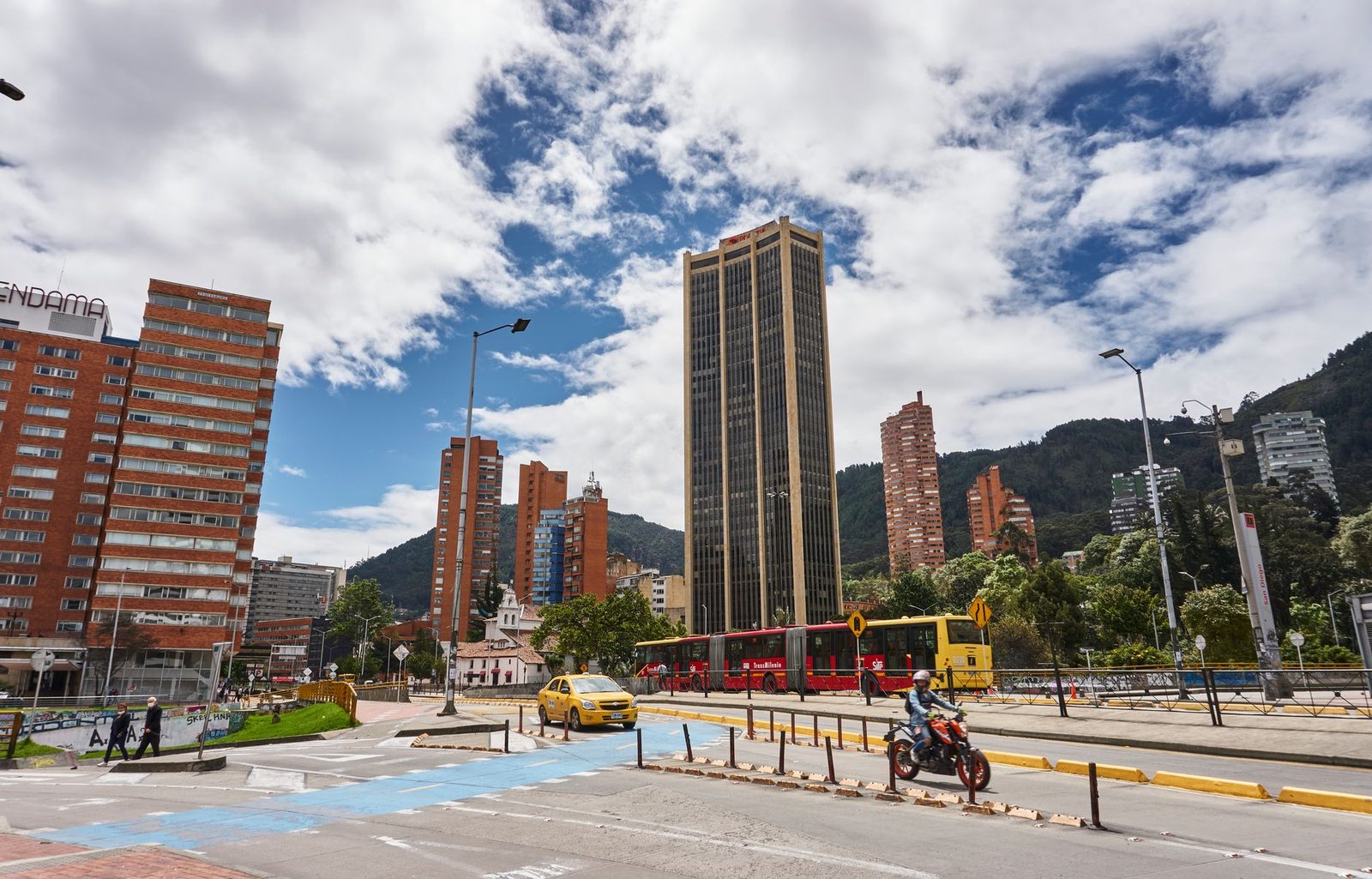 Calle concurrida de Bogotá con rascacielos y un autobús TransMilenio.