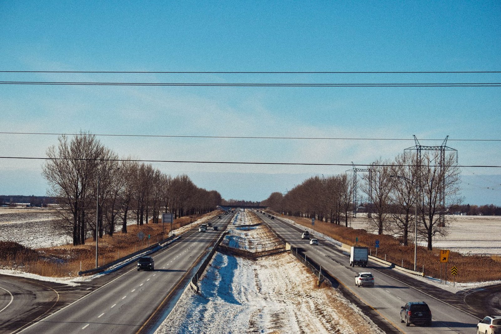 Coches y camiones circulan por una autopista nevada bajo un cielo azul despejado.
