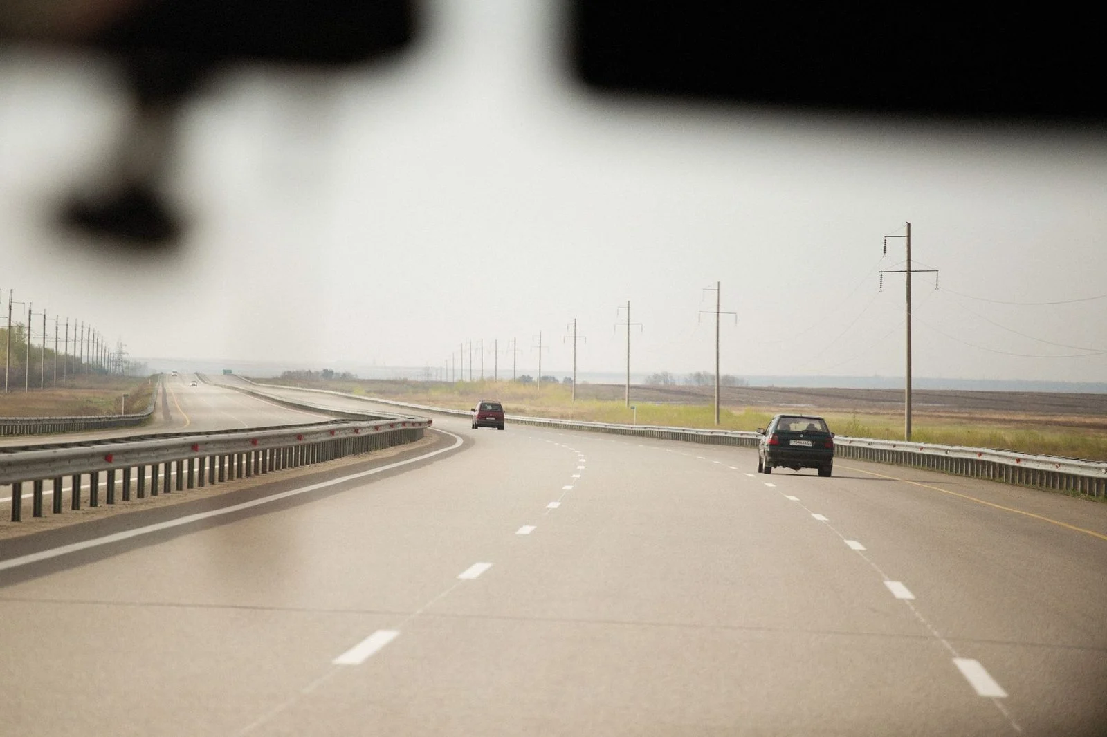 Cars travel along a wide highway past utility poles stretching into the distance.