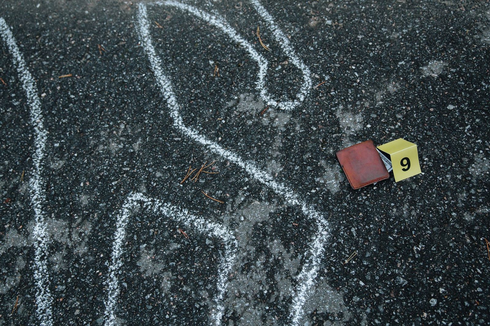 A chalk outline and numbered evidence markers on an asphalt street at a crime scene.