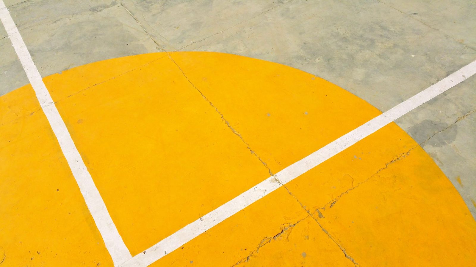 Close-up of a concrete basketball court with a yellow semicircle and white painted lines.