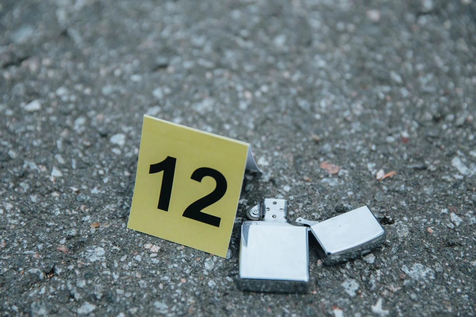 Close-up of a lighter beside a numbered evidence marker on a concrete surface at a crime scene.