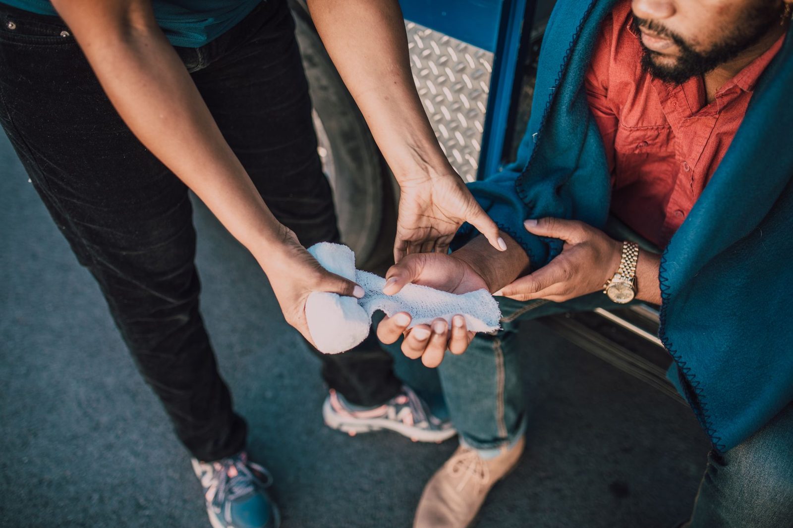Close-up of a person's hands applying gauze to a wound on another person's hand.