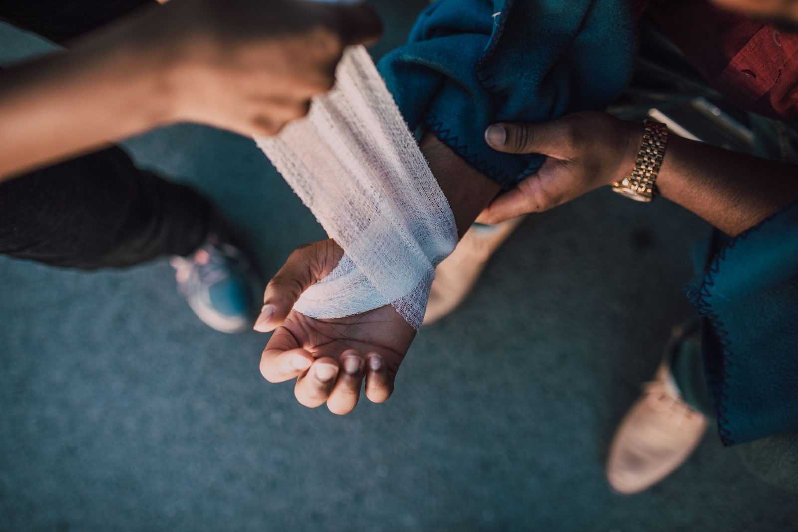 Close-up of hands wrapping a bandage around an injured wrist outdoors.