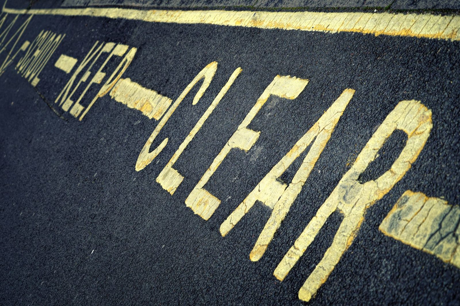 Primer plano de la señalización amarilla "KEEP CLEAR" pintada sobre el asfalto.