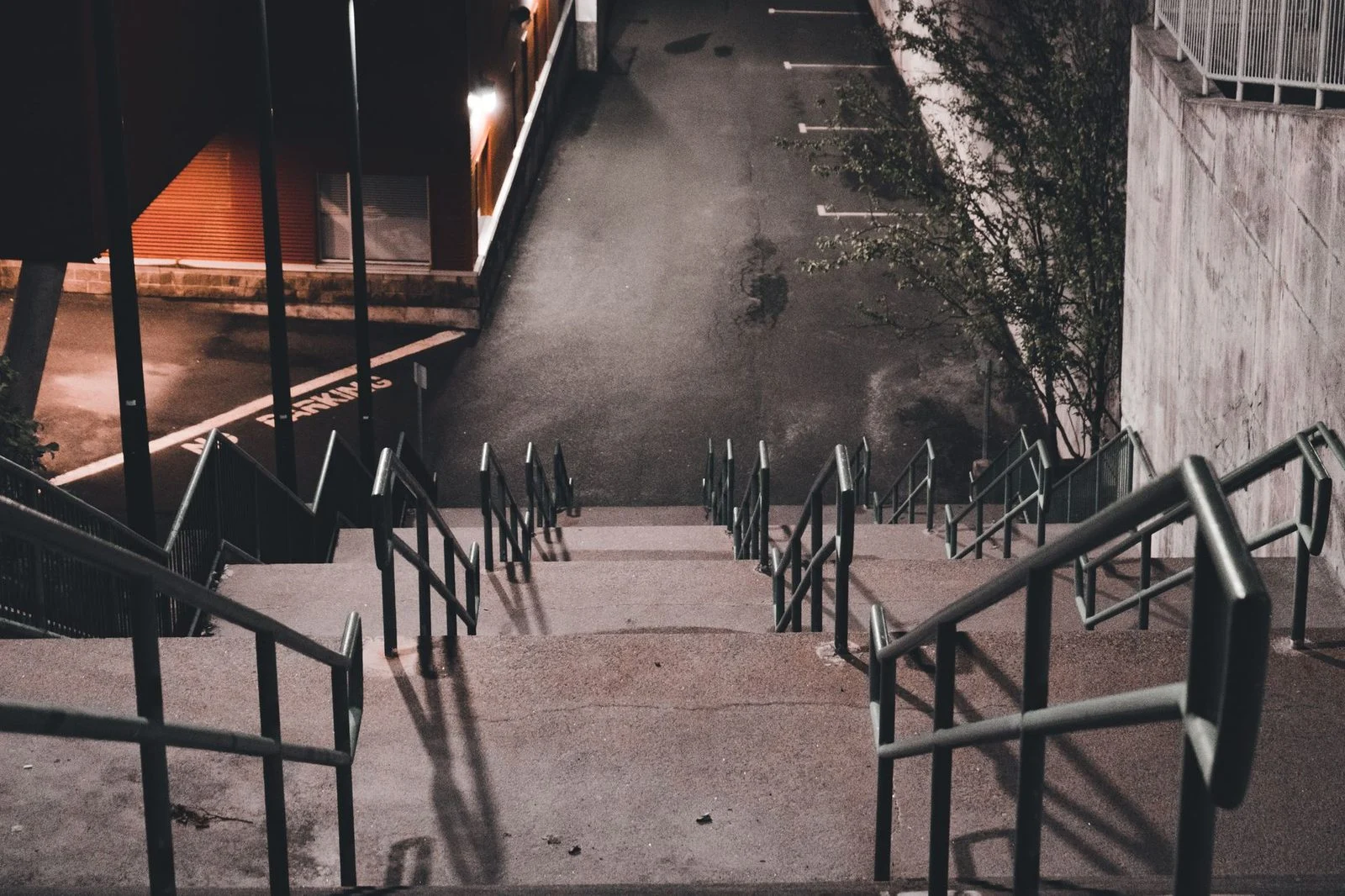 Empty concrete stairs with metal handrails descending into a dimly lit city alley at night.
