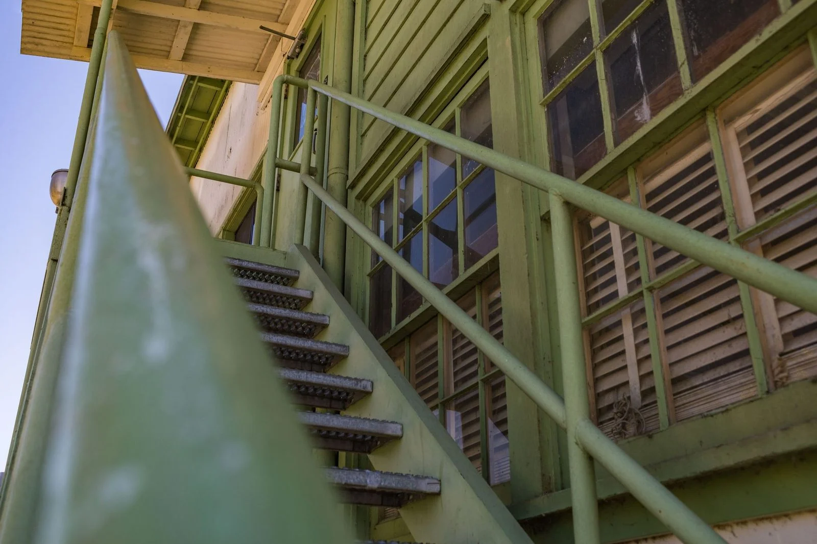Low-angle view of a green metal staircase beside the windowed exterior of an industrial building.