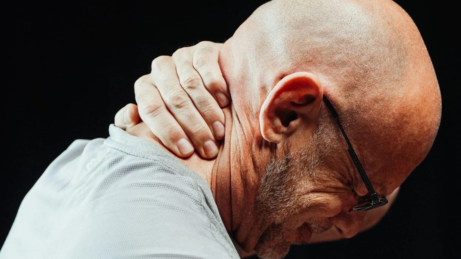 Hombre mayor de perfil sujetándose la nuca con gesto de molestia.
