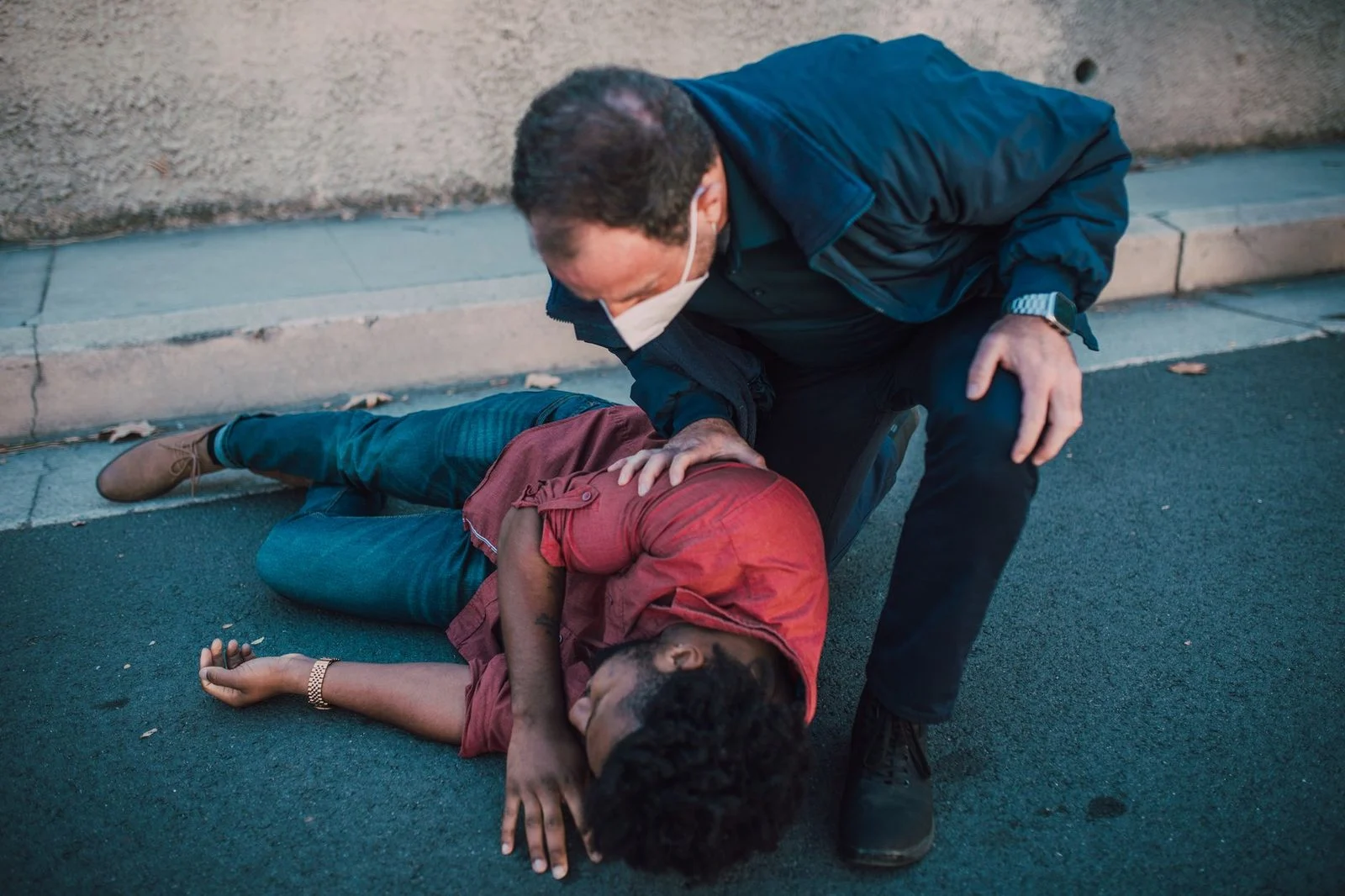 A paramedic kneeling beside an injured man lying on the roadside, providing emergency care.