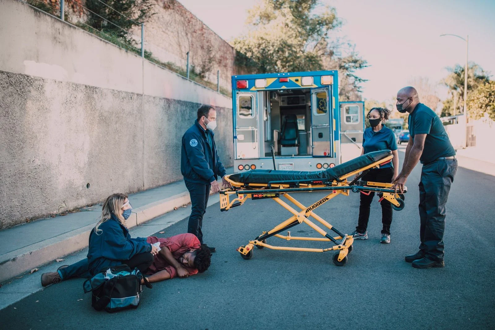 Paramedics attend to a patient beside an ambulance at the roadside.