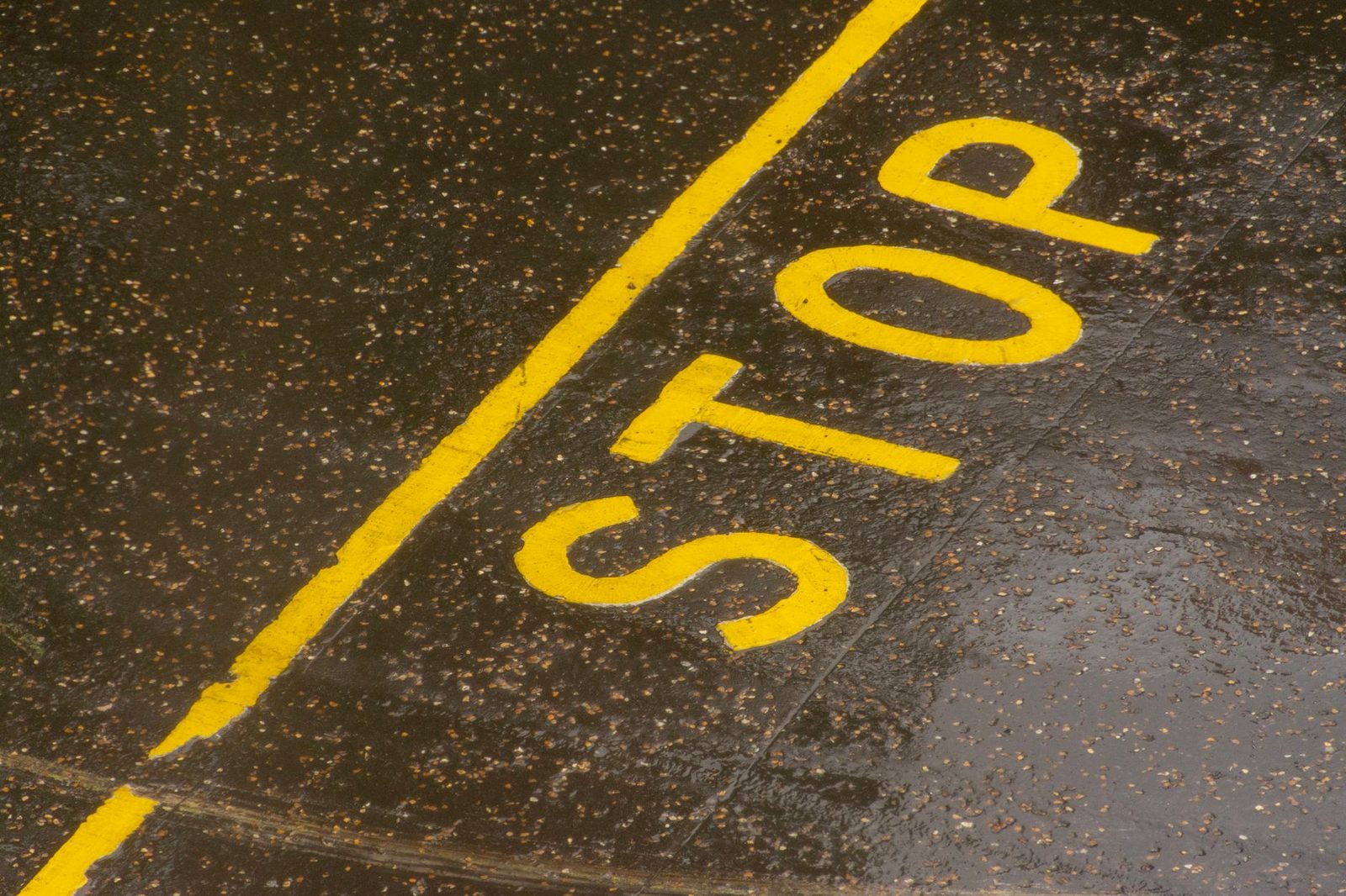 Rain-soaked road with a yellow painted STOP marking on the asphalt.