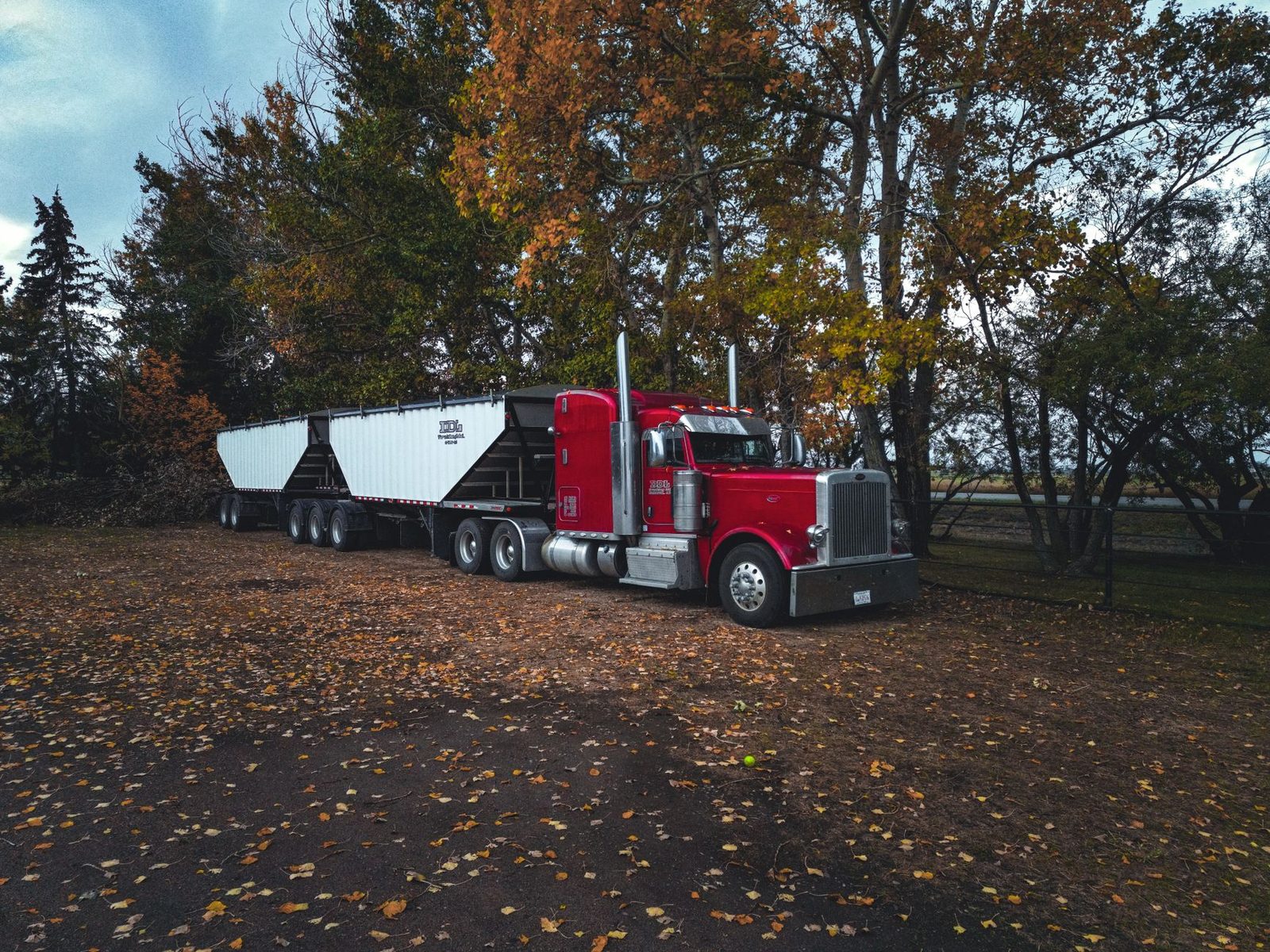 Red semi-trailer truck parked on a road surrounded by autumn trees