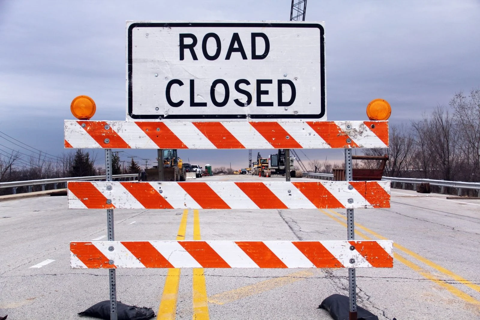 Señal de cierre de carretera y barrera en una autopista suburbana, indicando precaución.