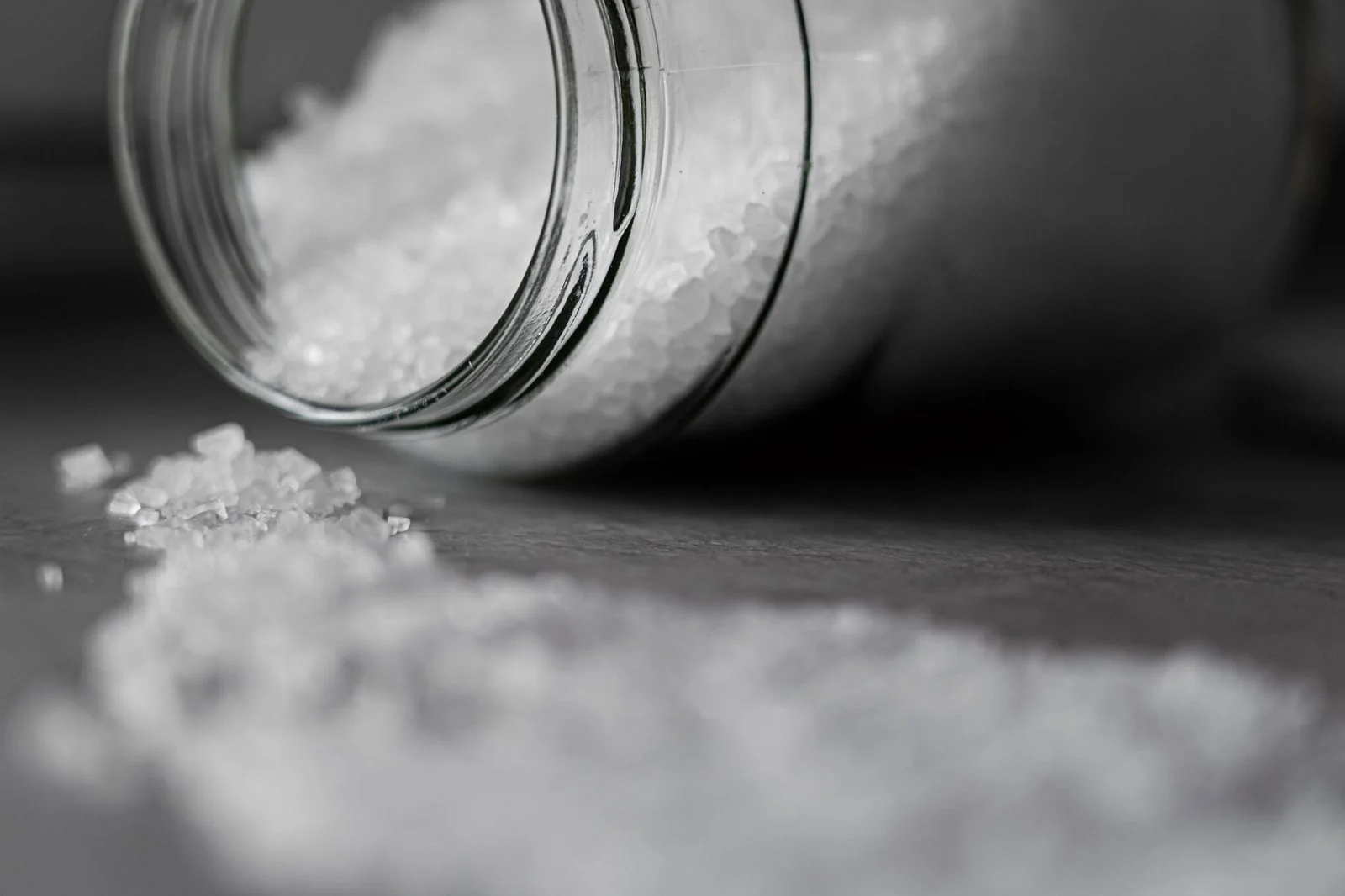 Rock salt spilling from a glass jar, with the foreground in sharp focus and the background blurred.