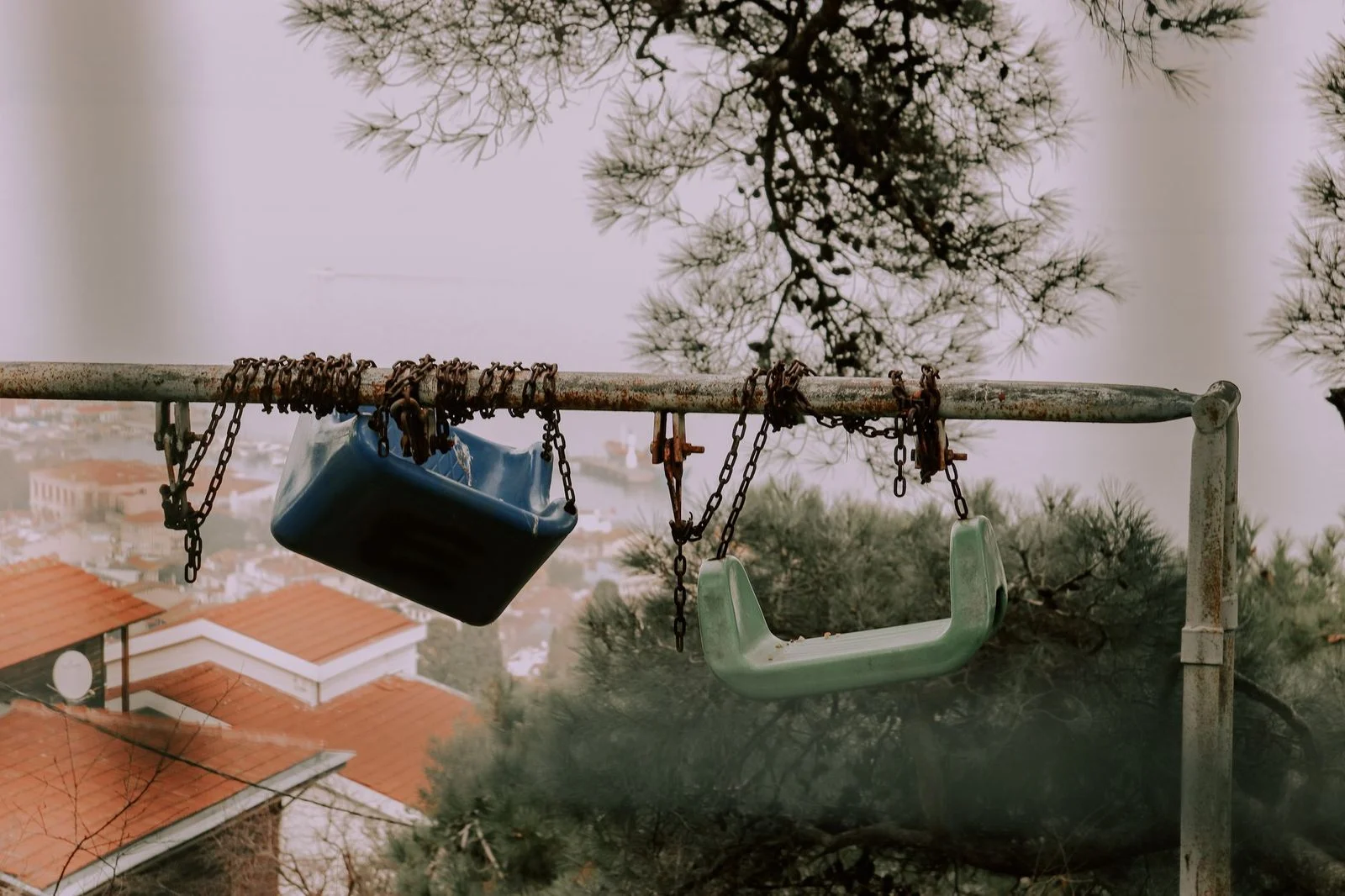 Rusted swing set with broken chains hanging from the frame, fading into misty trees.