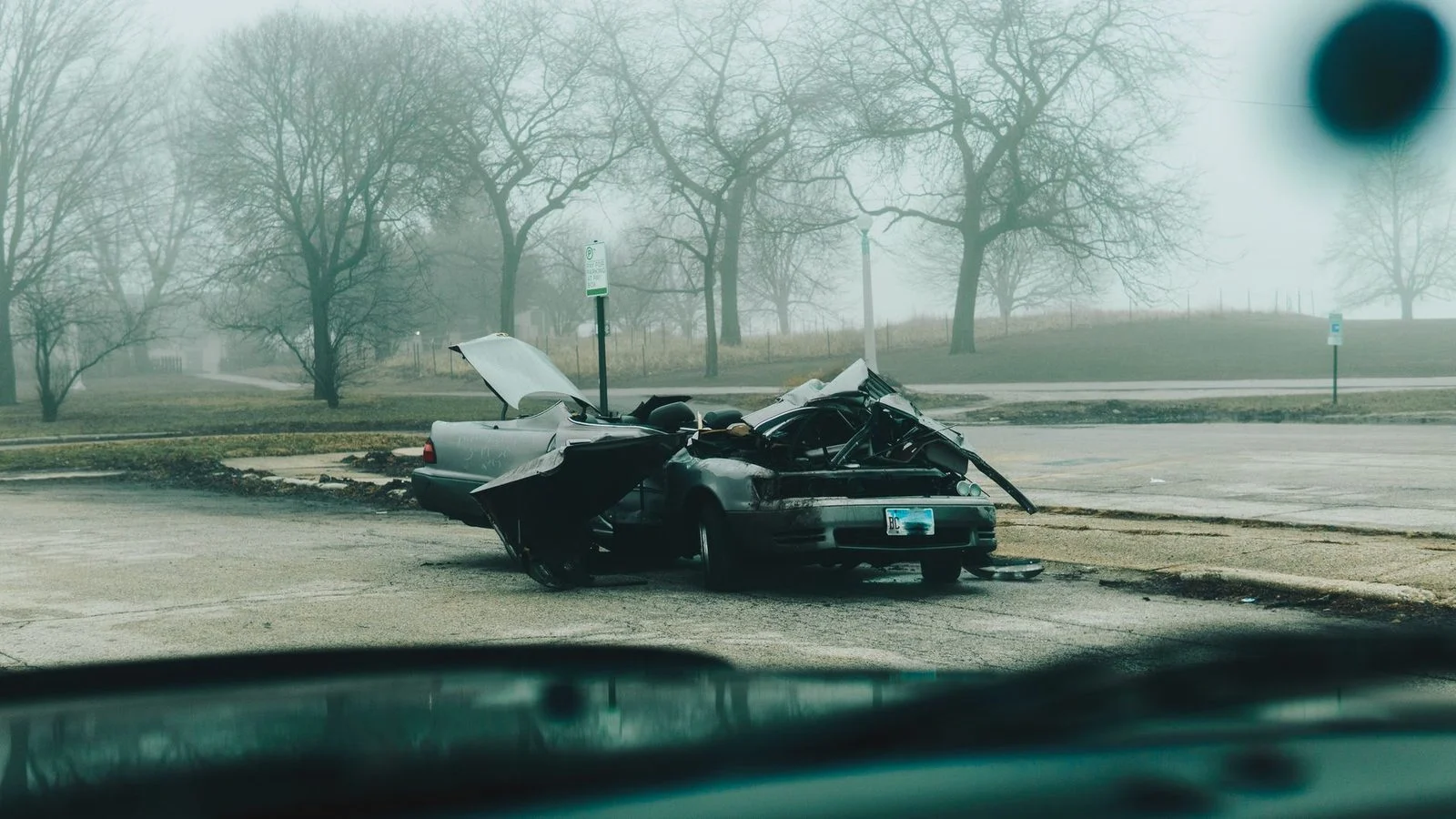 Severely damaged car on a deserted street during a foggy morning.