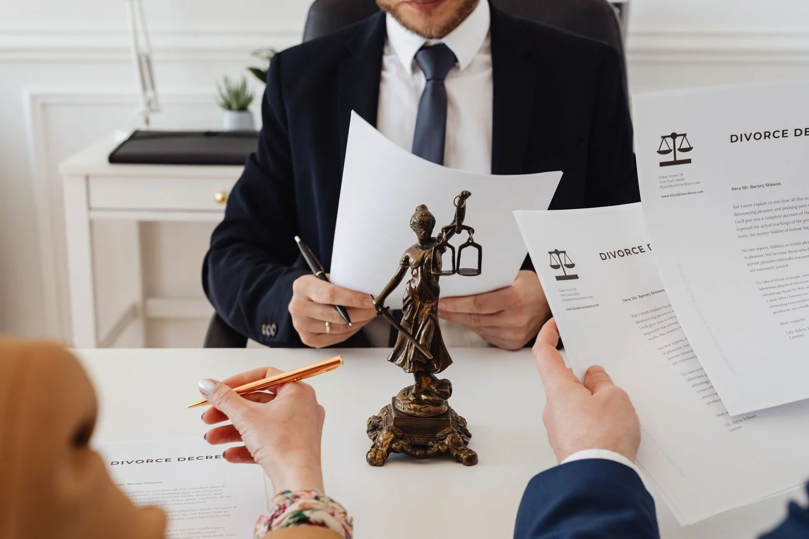 Two lawyers review divorce paperwork at a desk beside a Lady Justice statue in a law office.