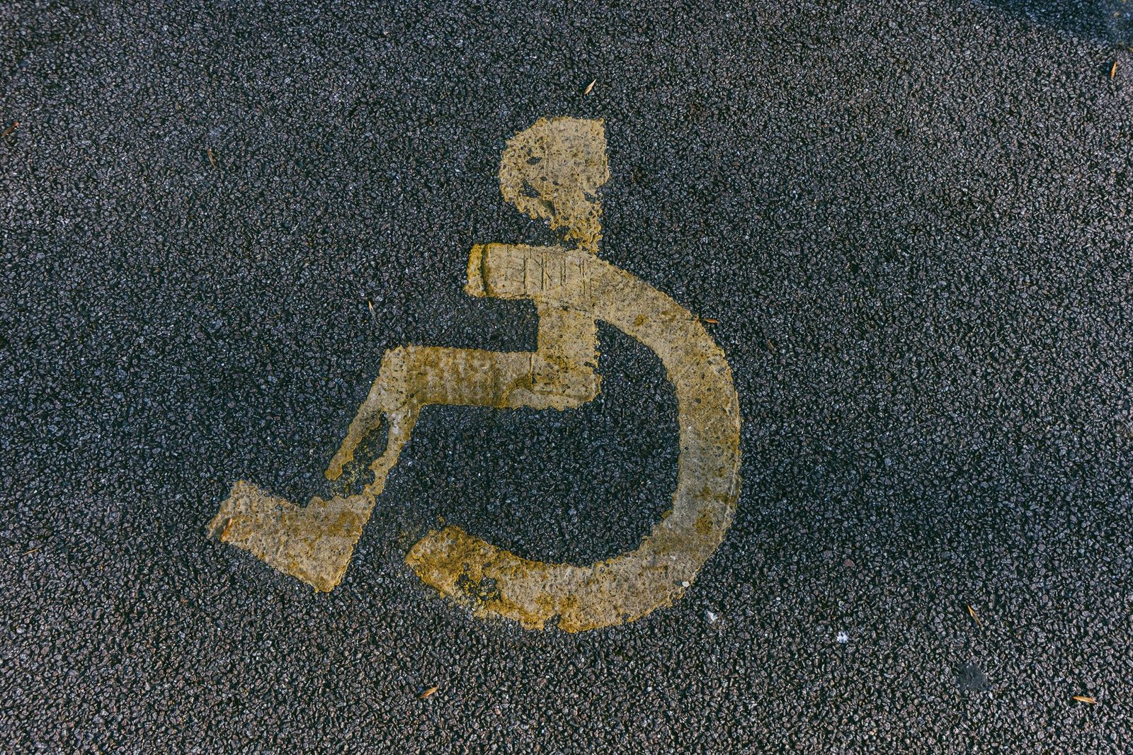 Weathered wheelchair access symbol painted on an asphalt parking space.