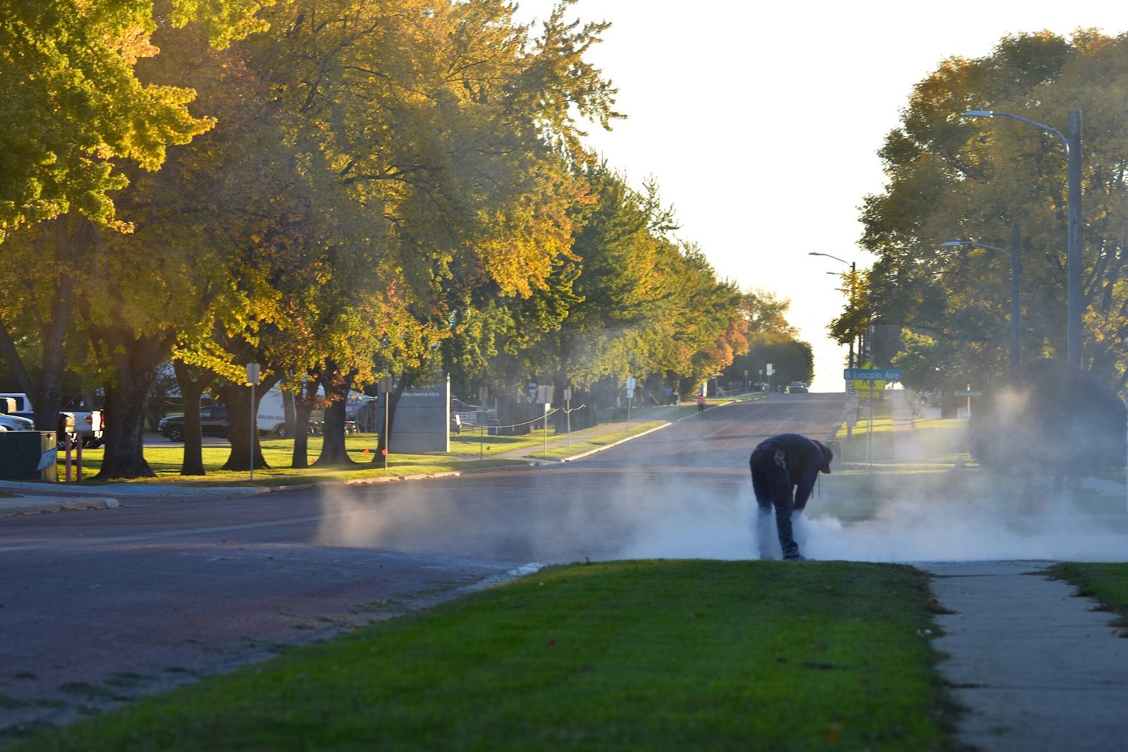 Trabajador cortando concreto en una calle arbolada una mañana soleada de otoño.