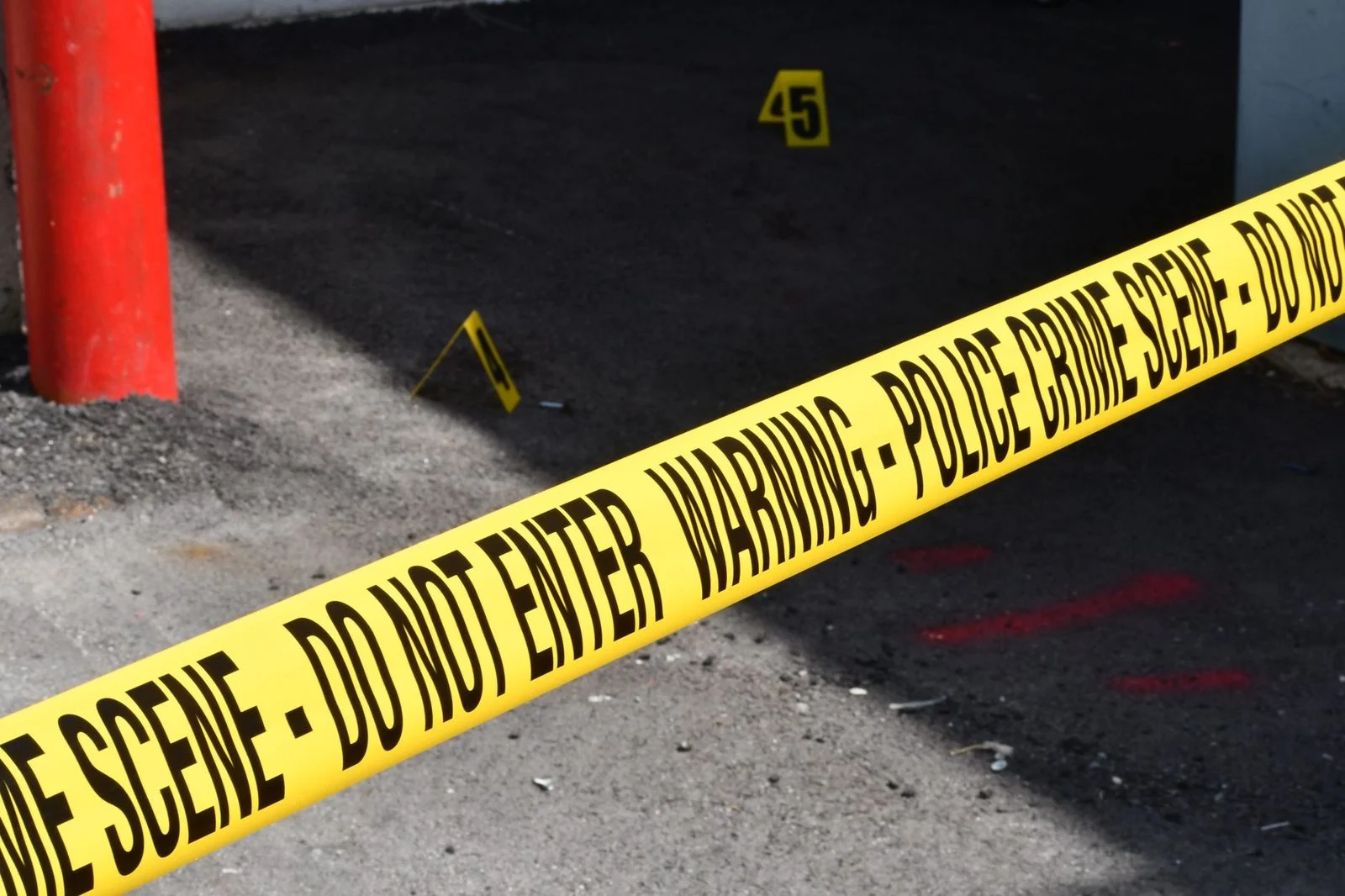 Yellow police crime scene tape stretches across a restricted area on a concrete street.