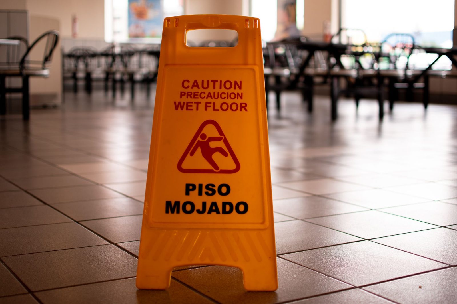 Un letrero amarillo de "piso mojado" sobre un piso de baldosas de cafetería, advirtiendo sobre superficies resbaladizas.